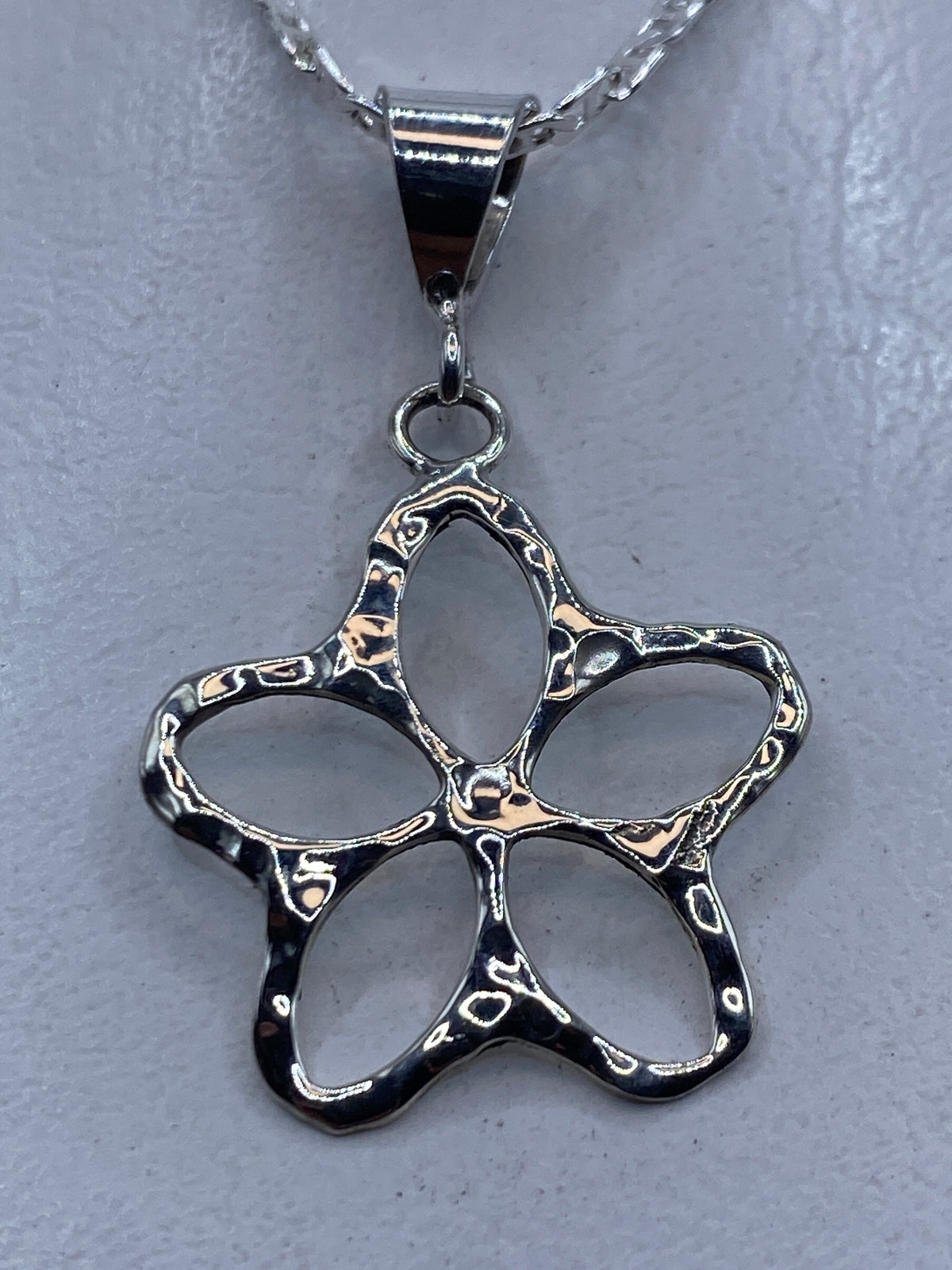 Dije de plata calado en forma de flor de cinco pétalos sobre cadena de plata