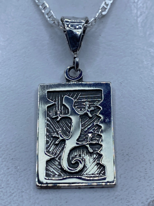 Dije prehispánico en plata repujada mostrando motivos aztecas y líneas ancestrales