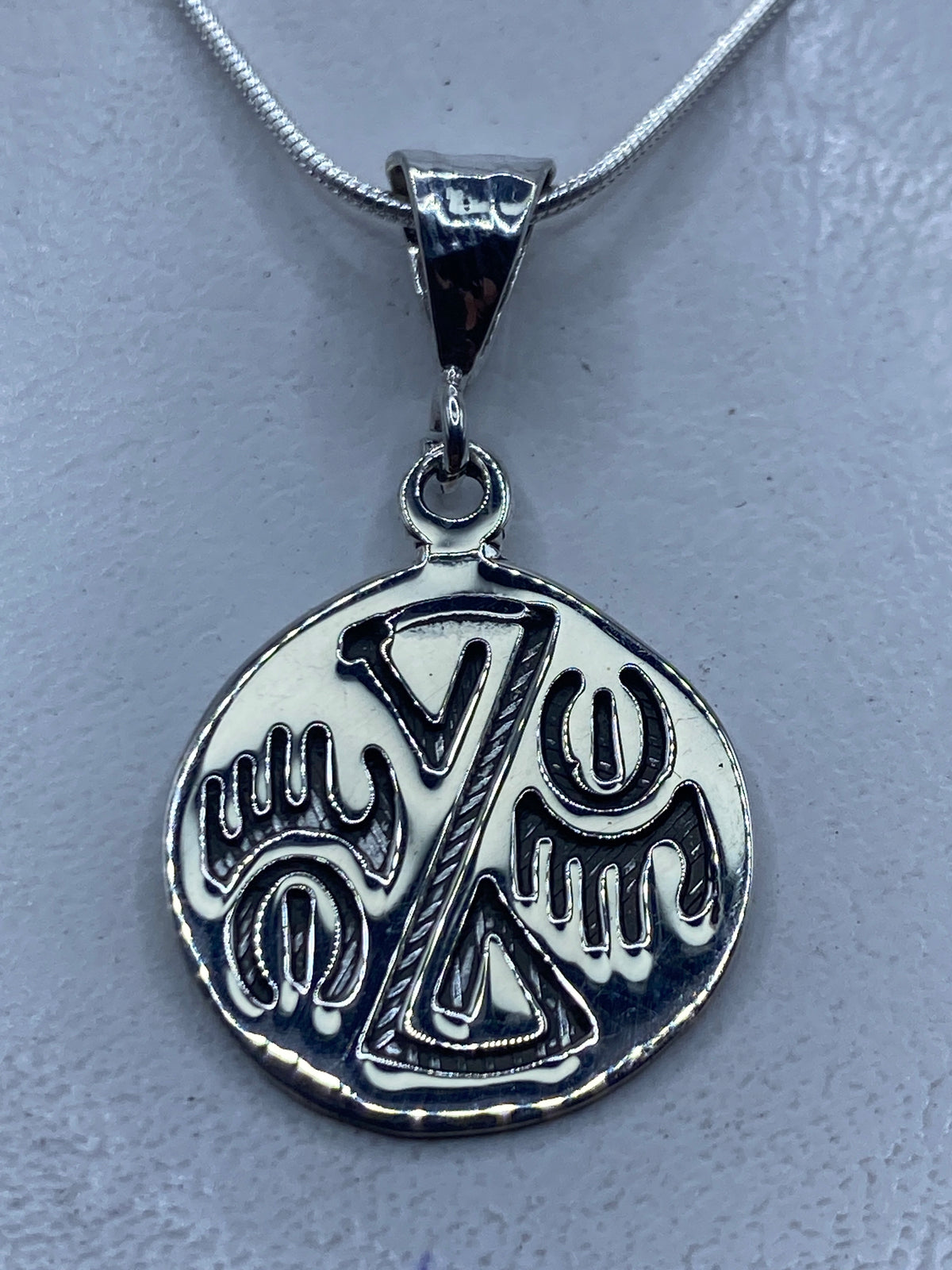 Dije de plata repujado con diseño prehispánico, colgado de cadena de plata en el cuello