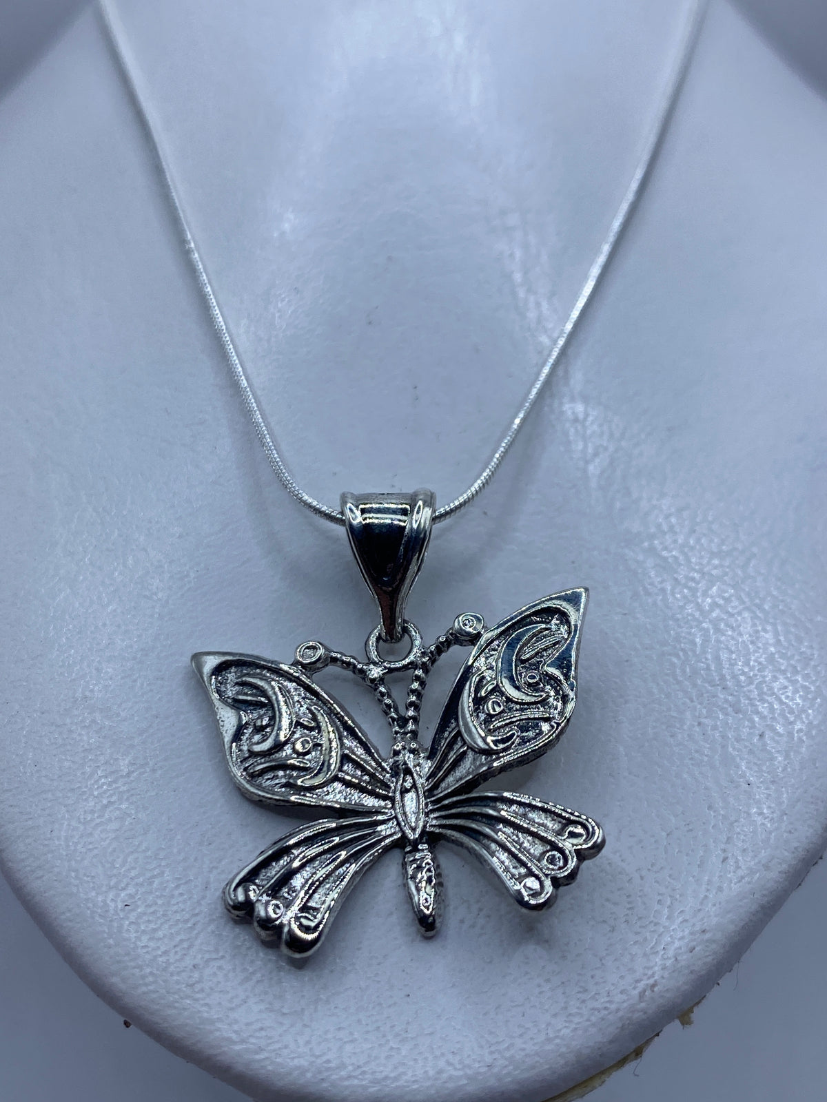 Detalle frontal del dije mariposa mostrando el relieve del repujado en las alas