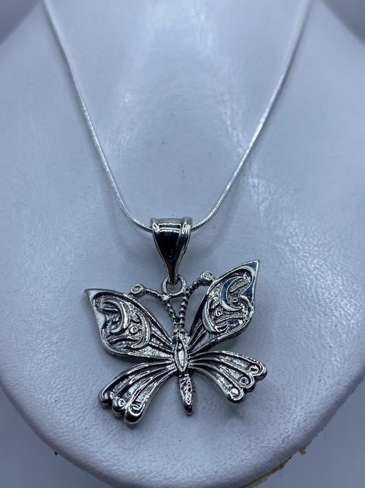 Detalle frontal del dije mariposa mostrando el relieve del repujado en las alas