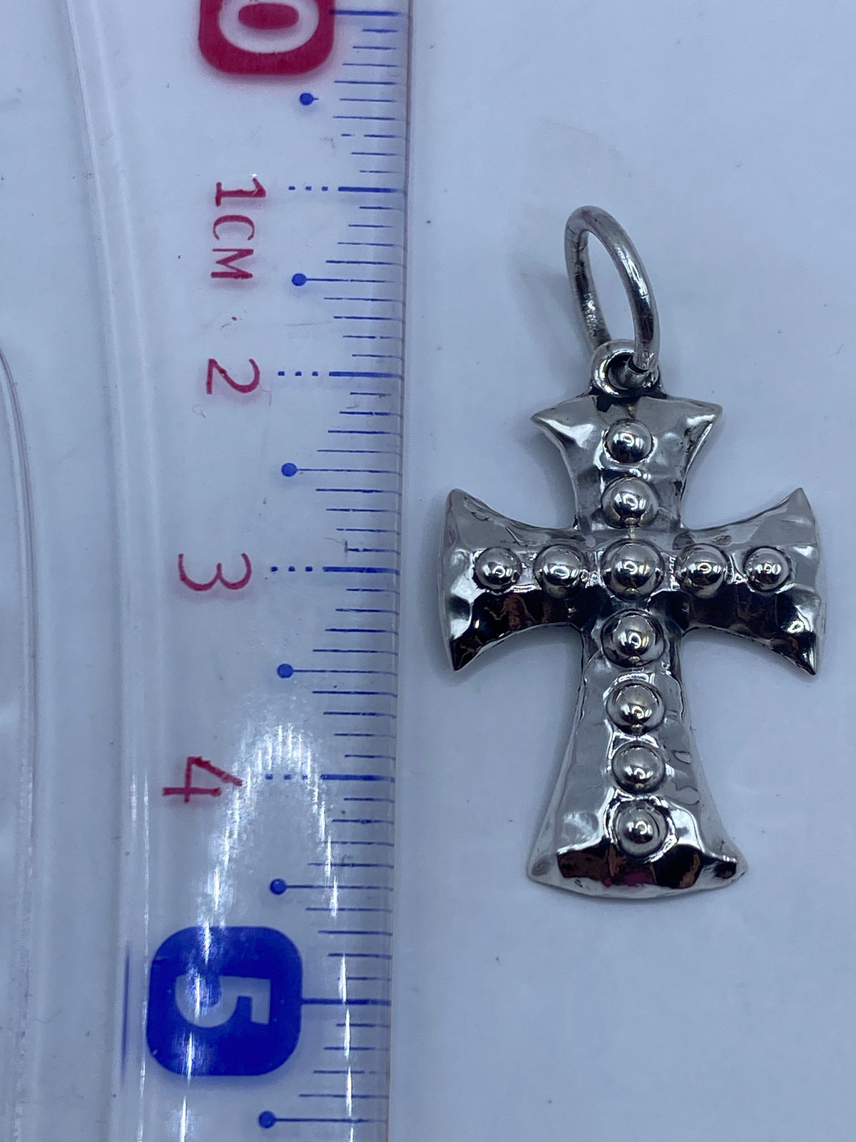 Dije cruz de plata sobre fondo blanco mostrando la textura y el Quinto .925