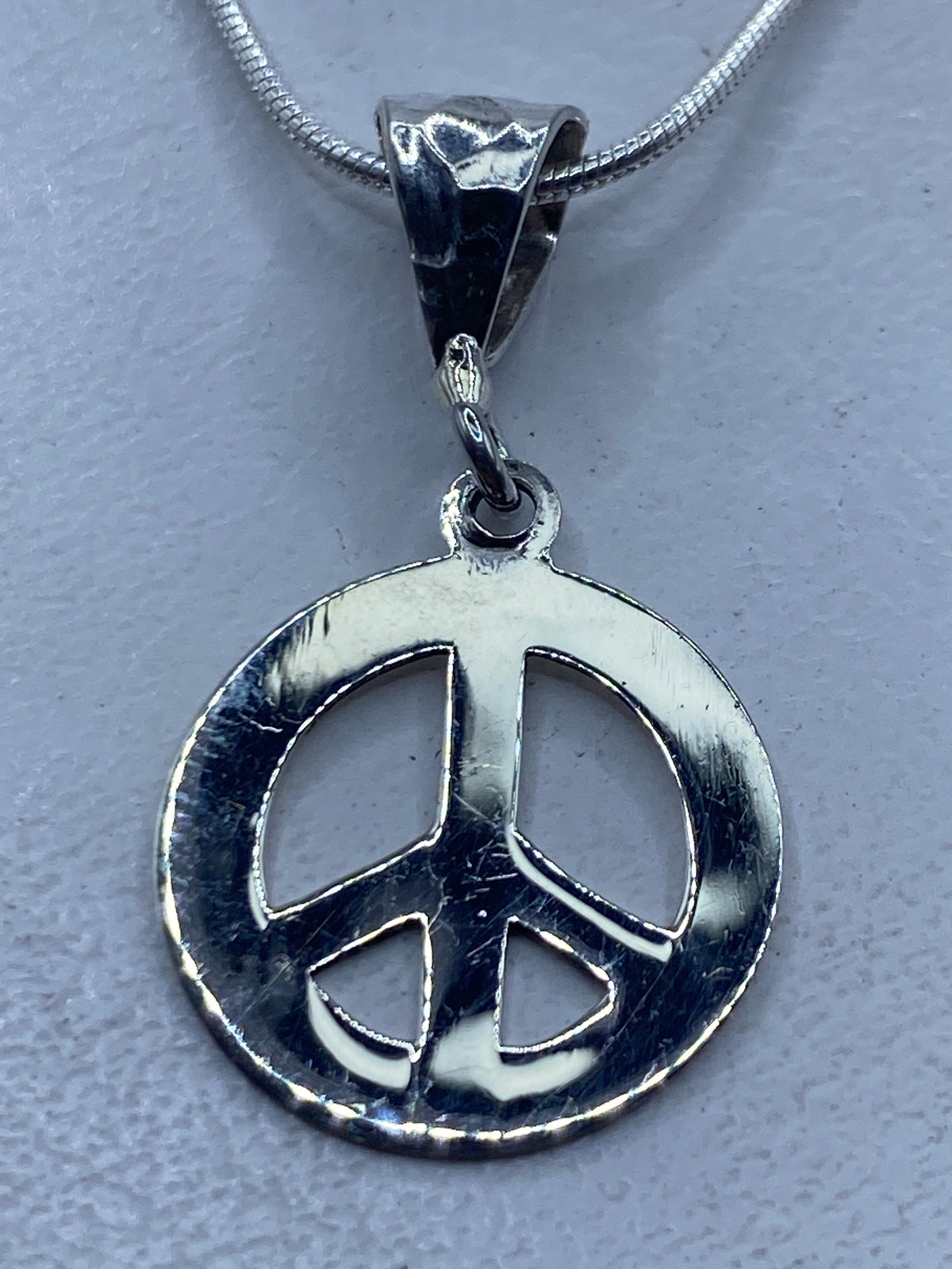 Dije de símbolo de paz en plata .925, colgando de una cadena de serpentina