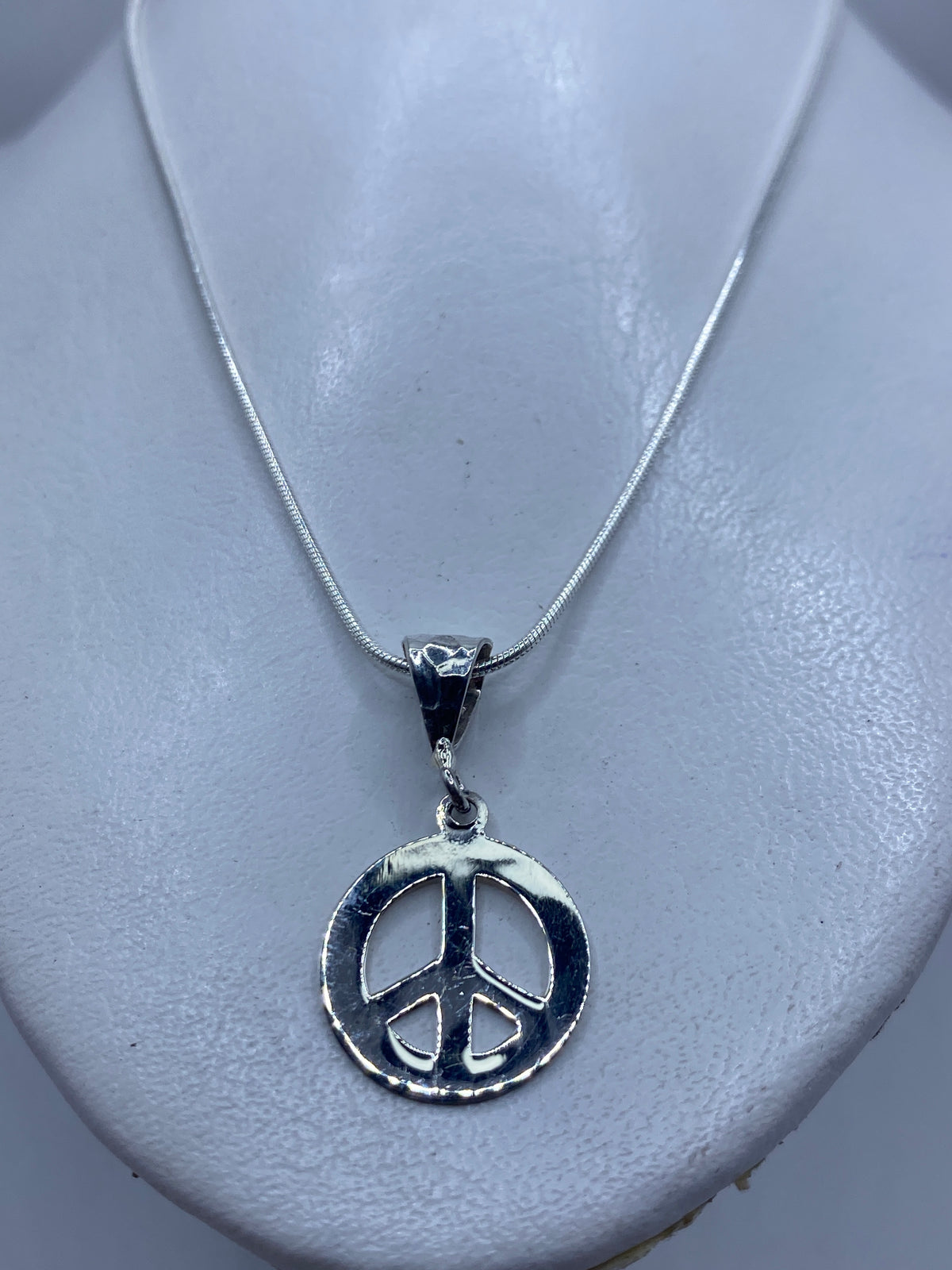 Detalle frontal del dije con símbolo de paz grabado, 3.7 cm de largo