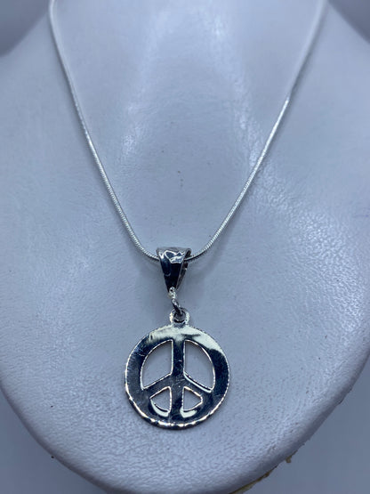 Detalle frontal del dije con símbolo de paz grabado, 3.7 cm de largo