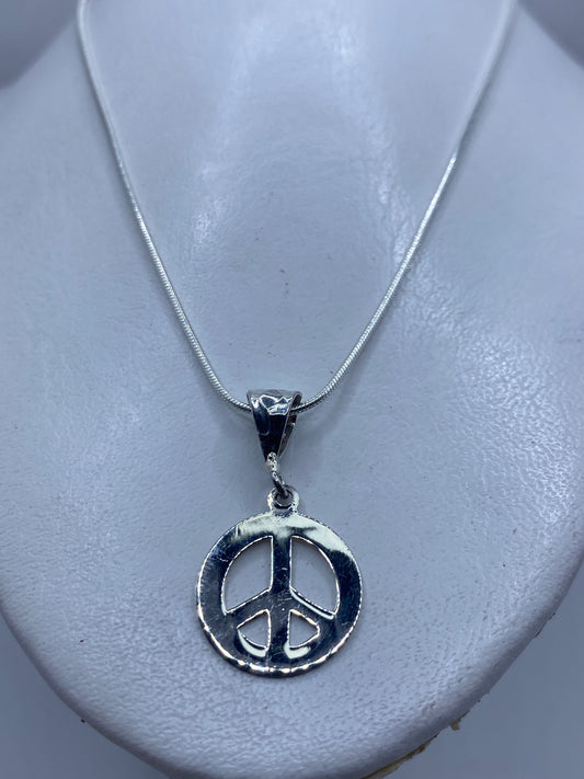 Detalle frontal del dije con símbolo de paz grabado, 3.7 cm de largo