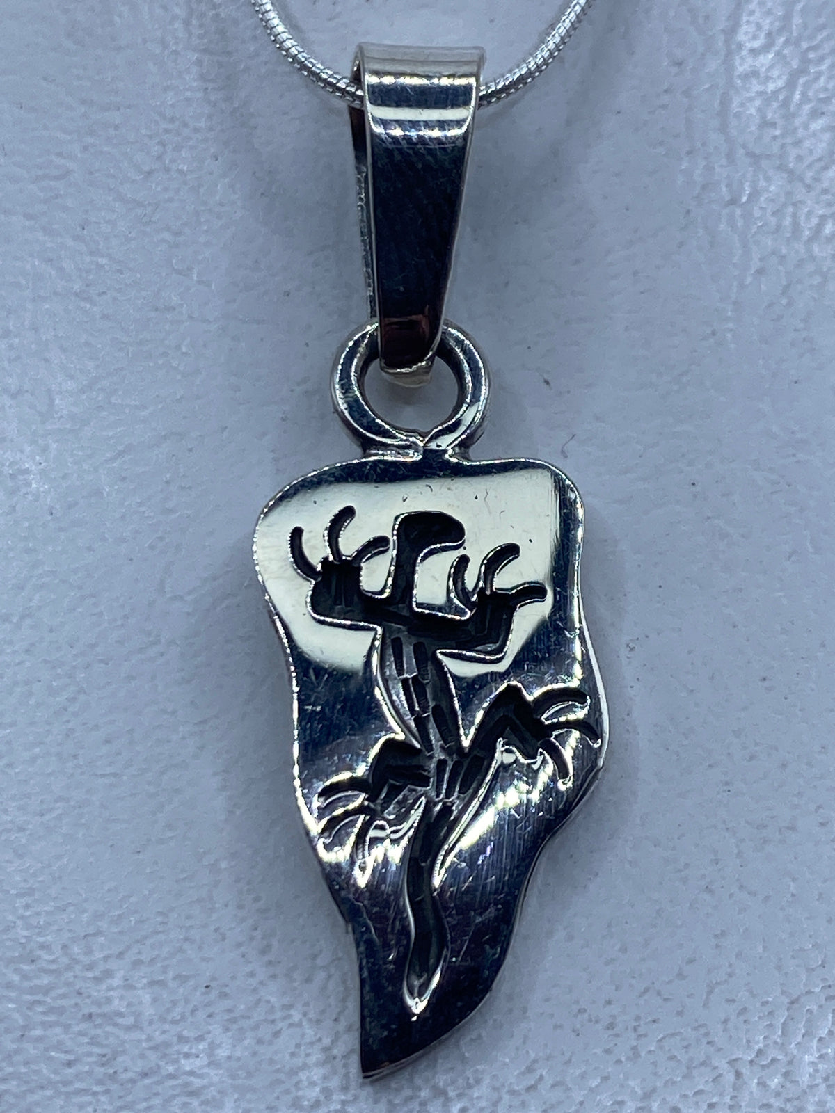 Dije de plata con motivo prehispánico en forma de guerrero, colgando de cadena plateada