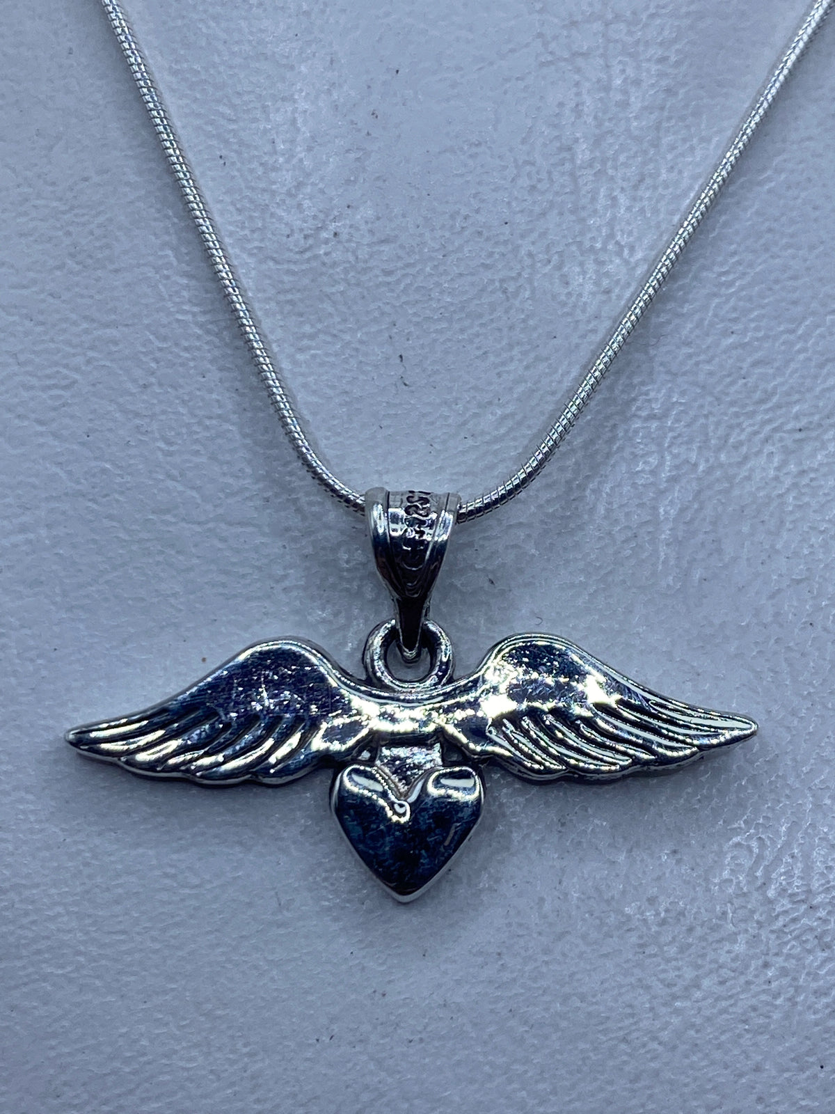Dije de plata con alas abiertas y corazón central, sobre collar de cadena serpiente