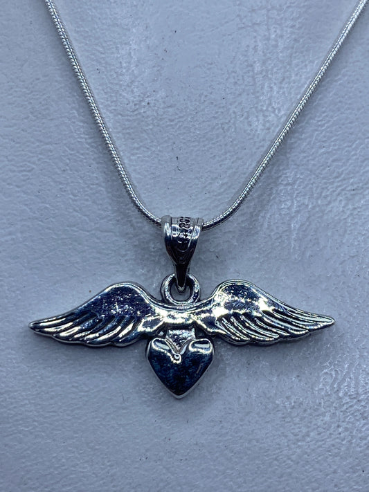 Dije de plata con alas abiertas y corazón central, sobre collar de cadena serpiente