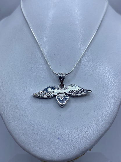 Detalle frontal del dije de alas y corazón mostrando el acabado pulido