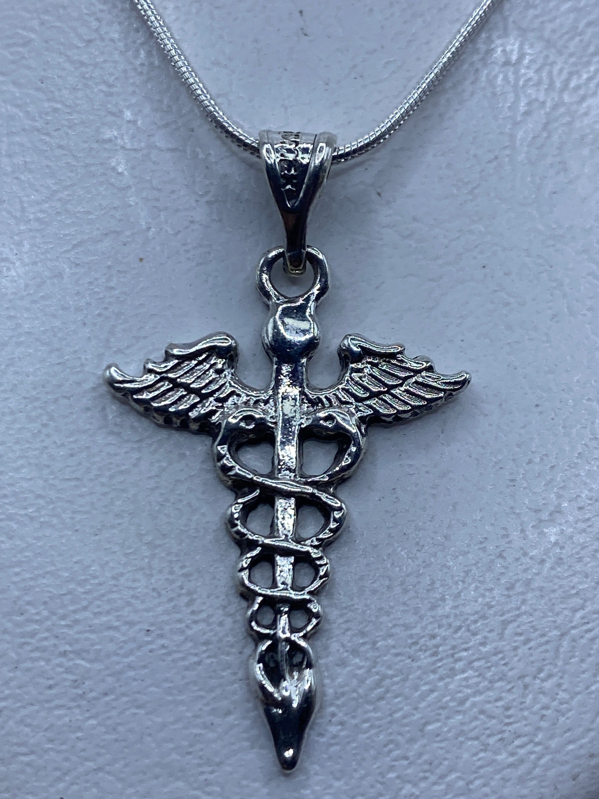 Dije Caduceo de plata .925 colgando de cadena serpentín, mostrando el símbolo médico en relieve