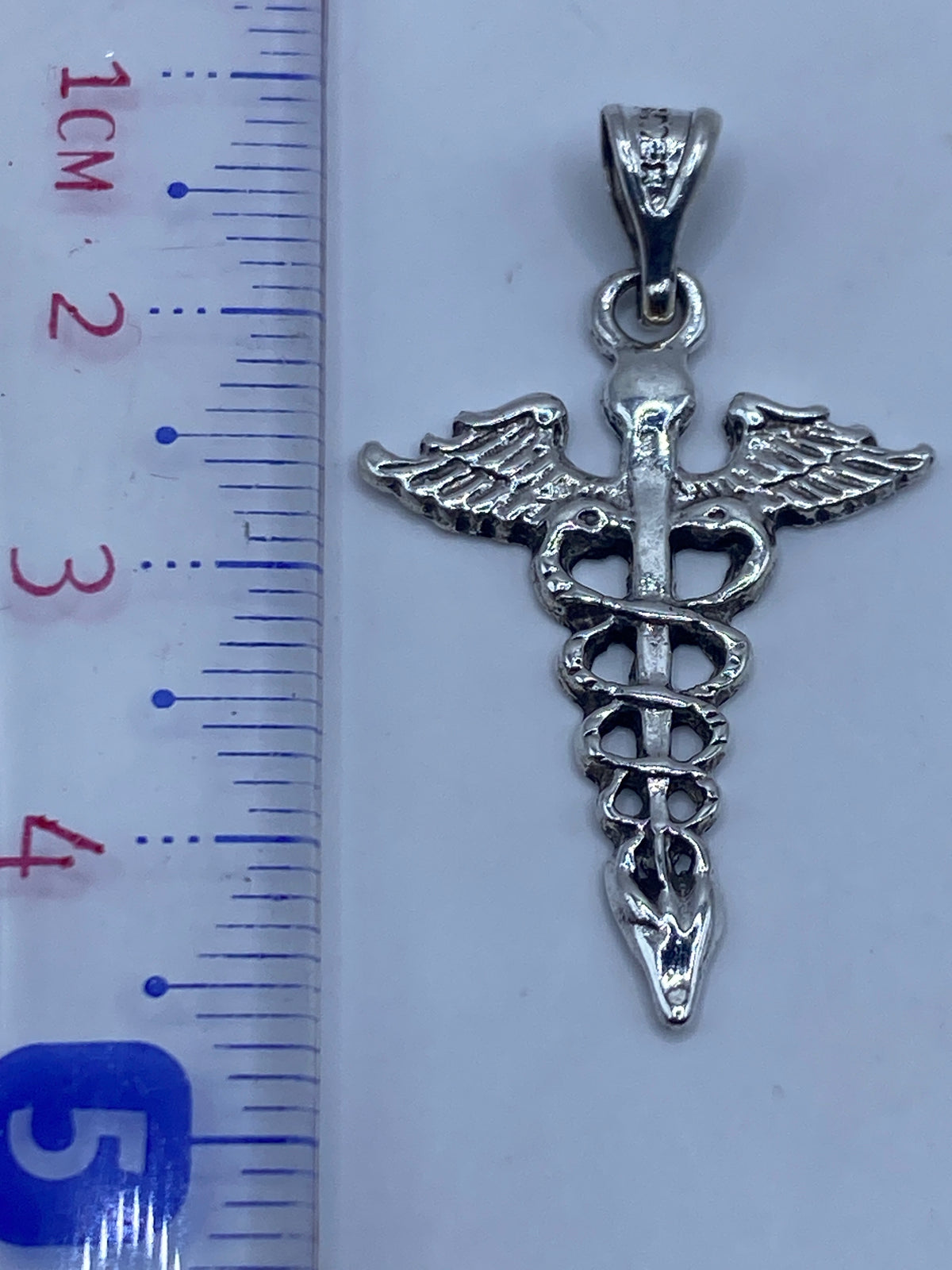 Dije Caduceo sobre fondo blanco, mostrando el acabado pulido y el Quinto .925 en la argolla