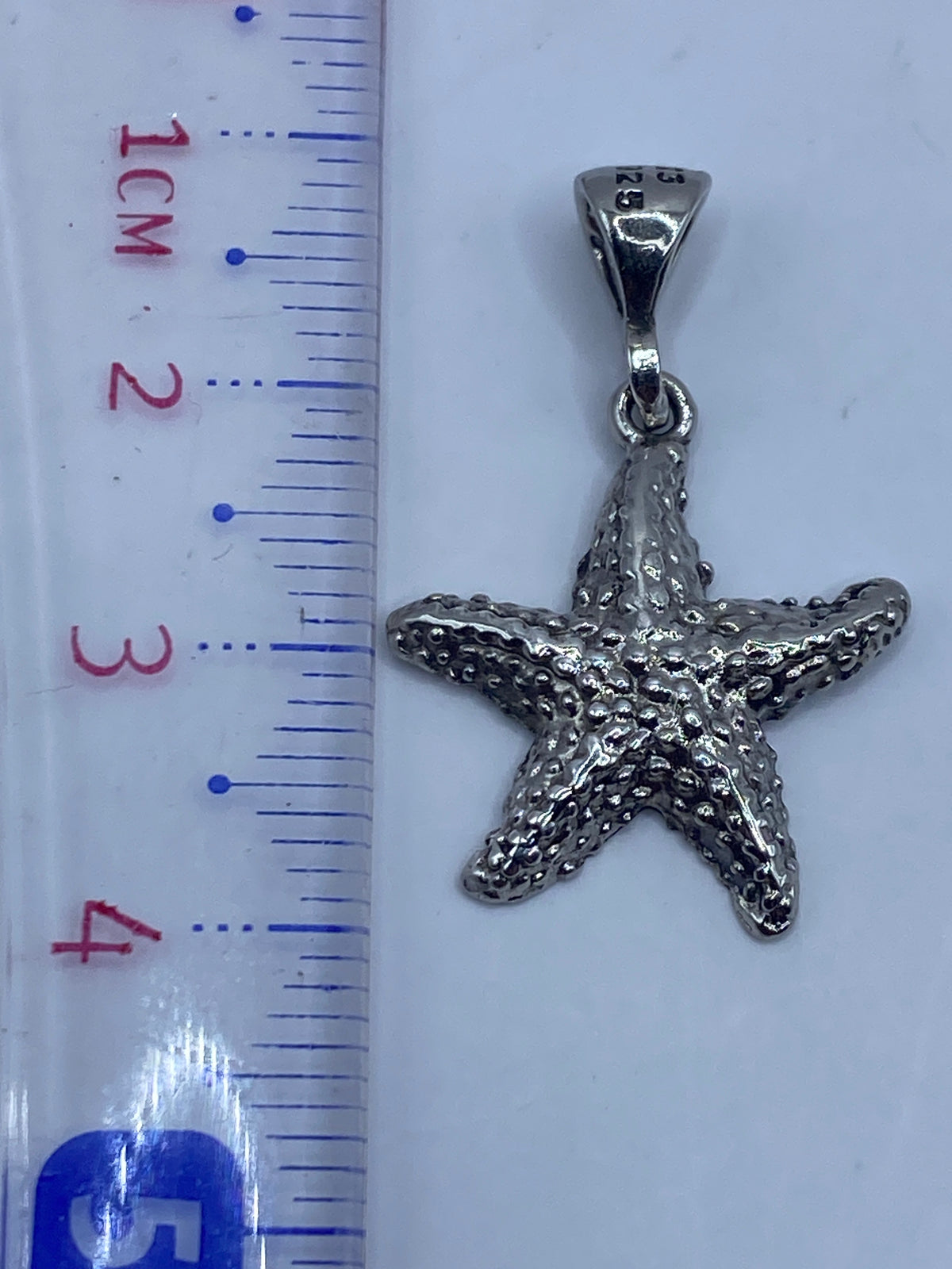 Dije estrella de mar de 3.7 cm en plata .925 sobre fondo neutro con escala de medida