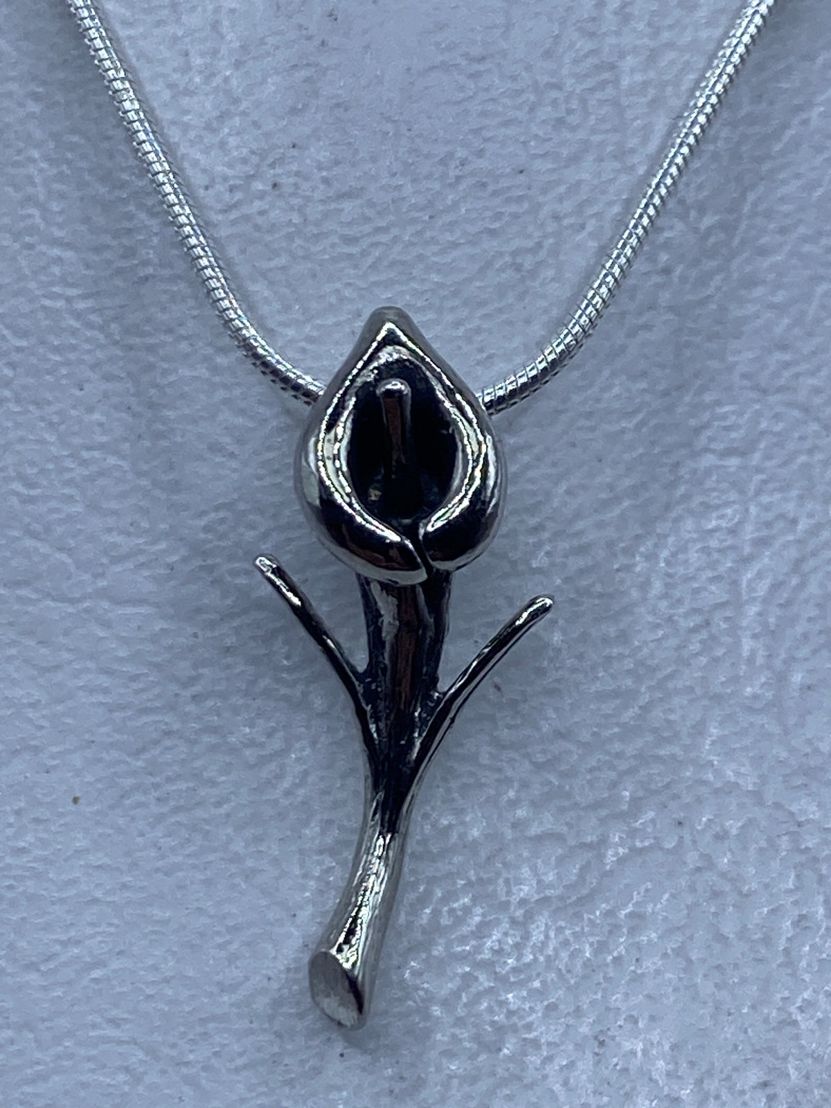 Dije de plata con forma de flor minimalista sobre cadena de plata, vista frontal