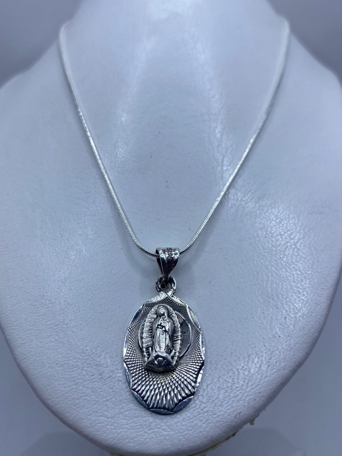 Detalle frontal del dije devocional mostrando la Virgen de Guadalupe y el halo radiante