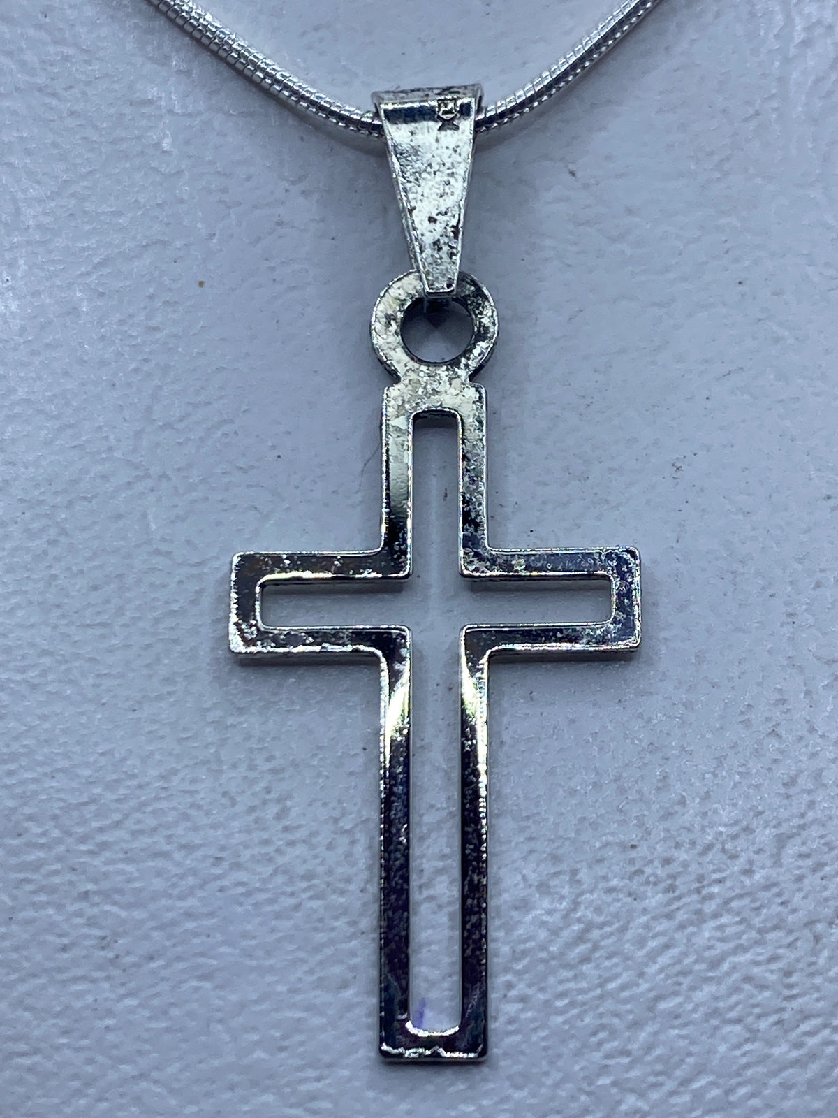 Cruz de plata calada 4.4 cm colgada en cadena fina de plata, sobre piel