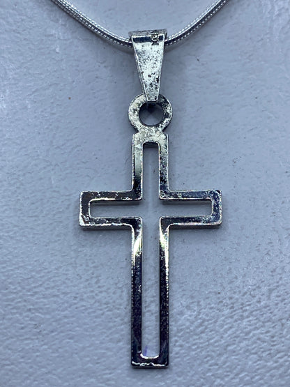 Cruz de plata calada 4.4 cm colgada en cadena fina de plata, sobre piel