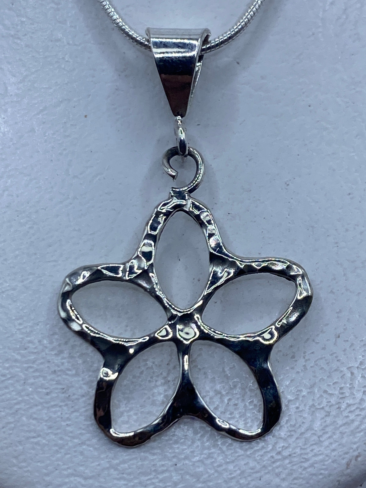 Dije de plata calado en forma de flor de cuatro pétalos sobre cadena de plata