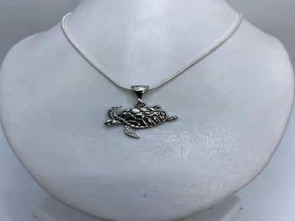 Dije de plata tortuga marina repujado colgando de cadena de plata sobre el pecho