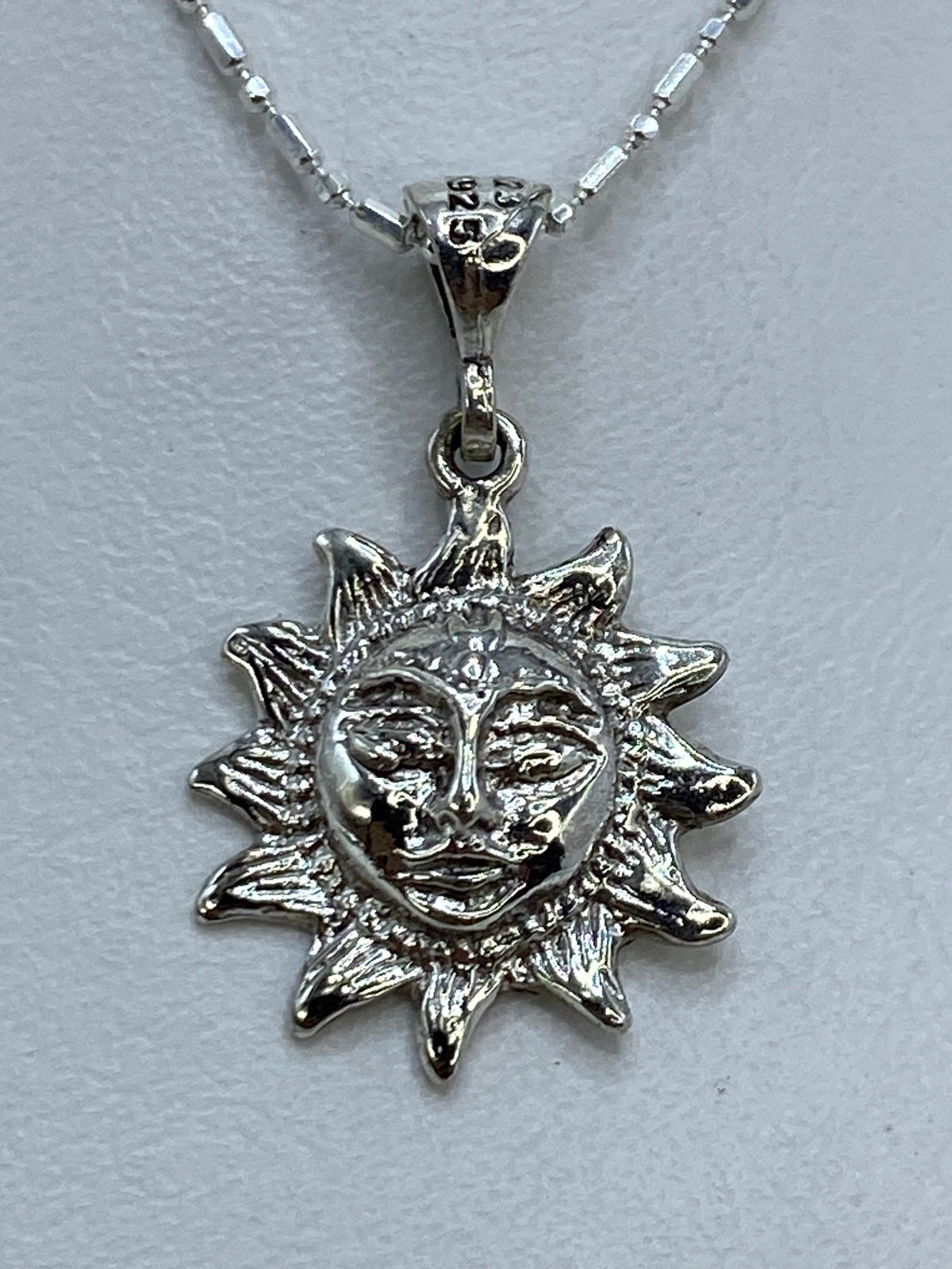 Dije de plata repujado en forma de sol con rostro artesanal, colgando de cadena delgada
