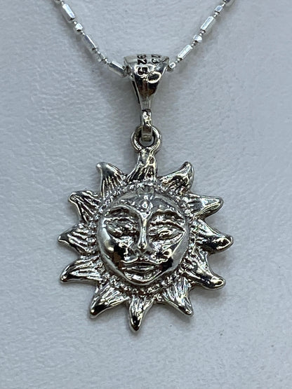 Dije de plata repujado en forma de sol con rostro artesanal, colgando de cadena delgada