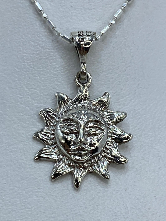 Dije de plata repujado en forma de sol con rostro artesanal, colgando de cadena delgada