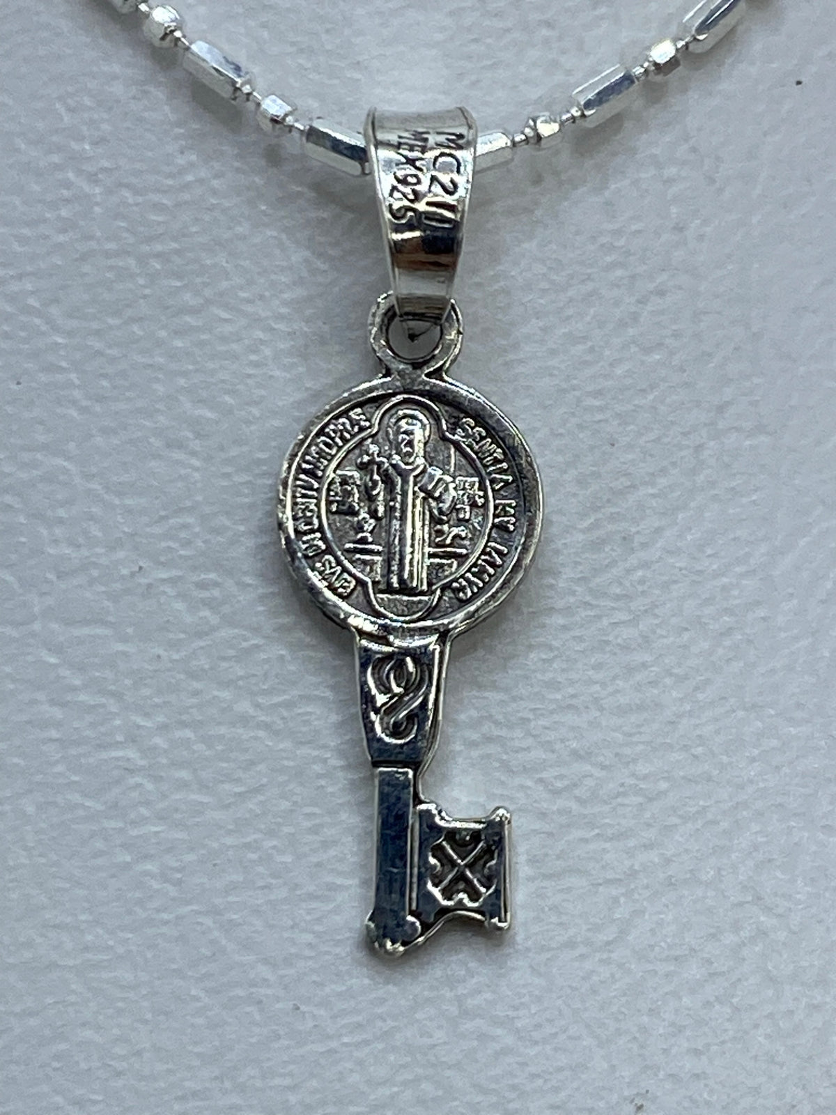 Dije de plata repujado con San Benito y llave en la palma de una mano