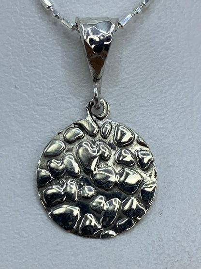 Dije de plata .925 repujado con textura orgánica, colgando de una cadena plateada