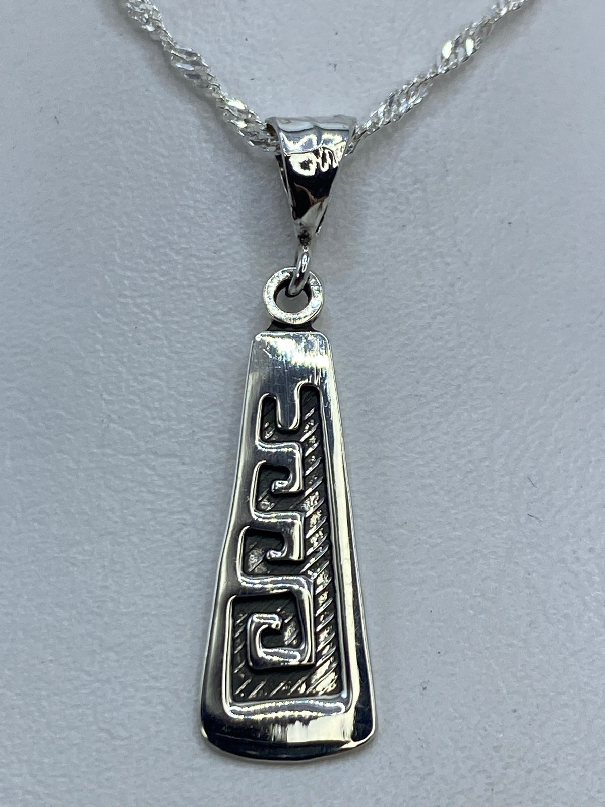 Dije de plata repujado con espiral prehispánica, 3 cm de largo, colgando de una cadena plateada