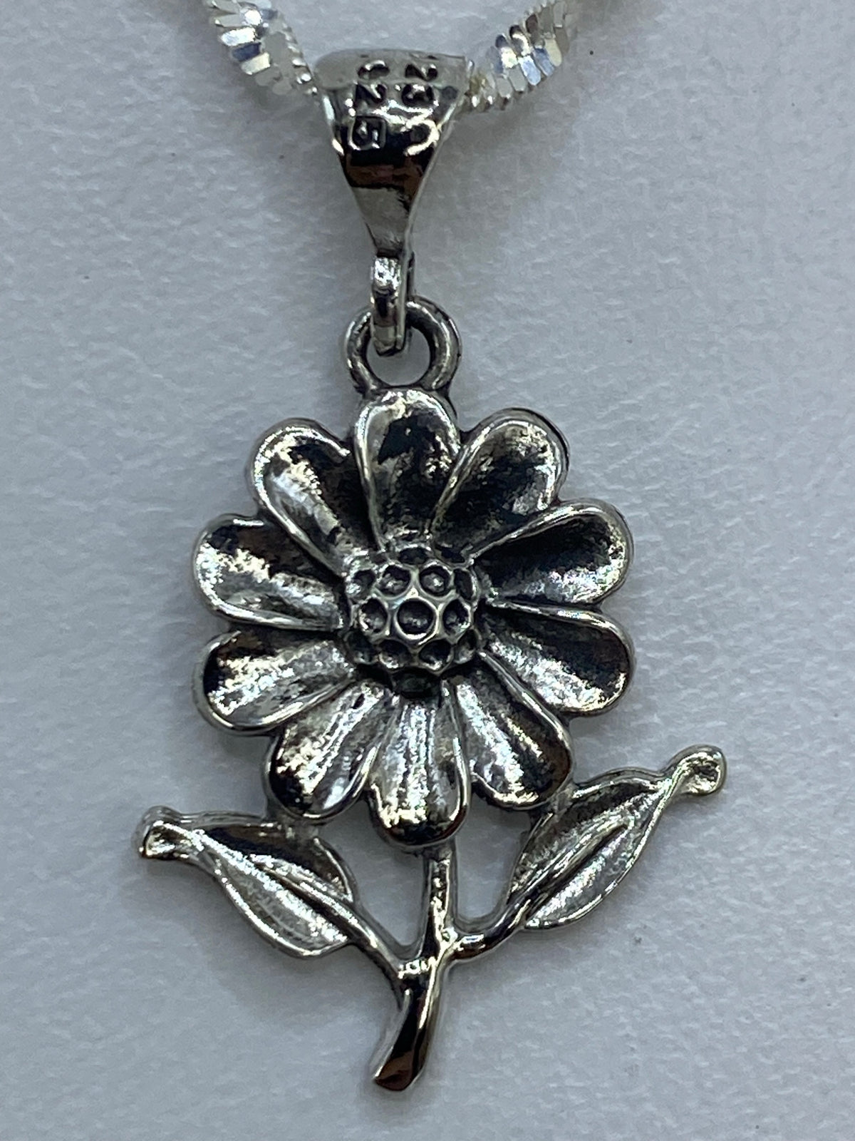 Dije flor con dos hojas en plata de Taxco sobre escala de medidas