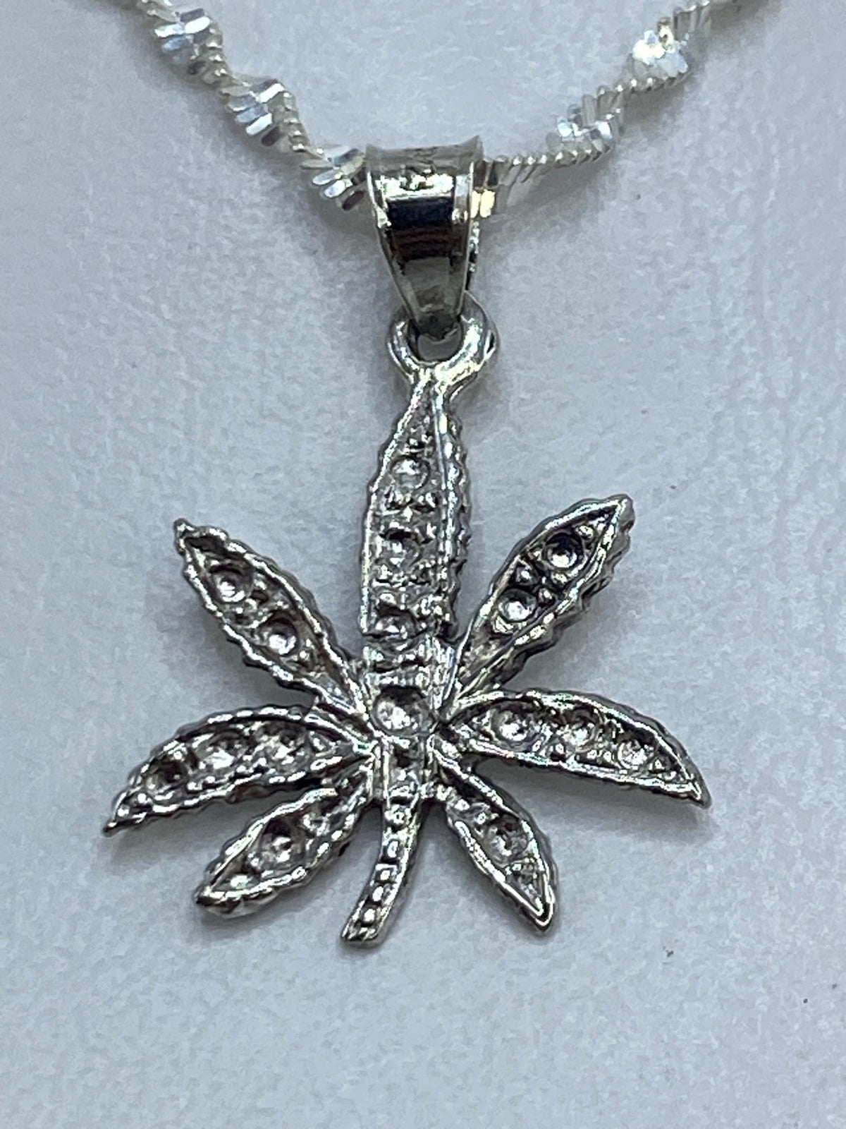 Dije de plata repujado con forma de hoja de marihuana en relieve, colgante sobre fondo blanco