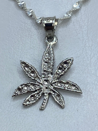 Dije de plata repujado con forma de hoja de marihuana en relieve, colgante sobre fondo blanco