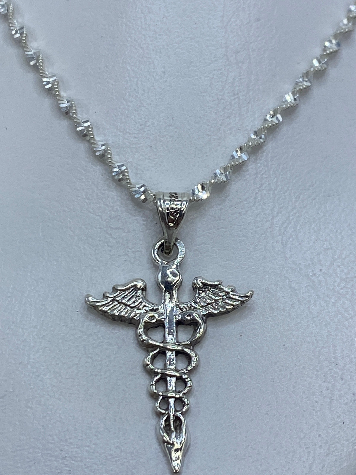 Detalle del caduceo en plata mostrando las serpientes y el bastón central