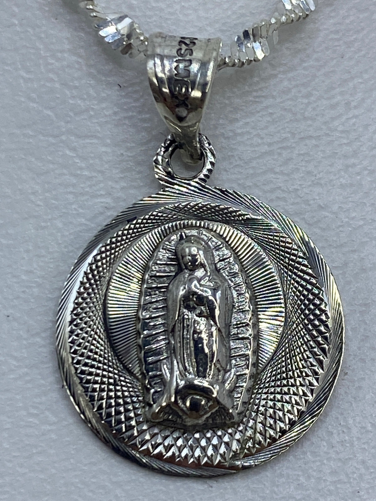 Dije de Virgen de Guadalupe en escala junto a regla métrica, mostrando tamaño real de 2 cm