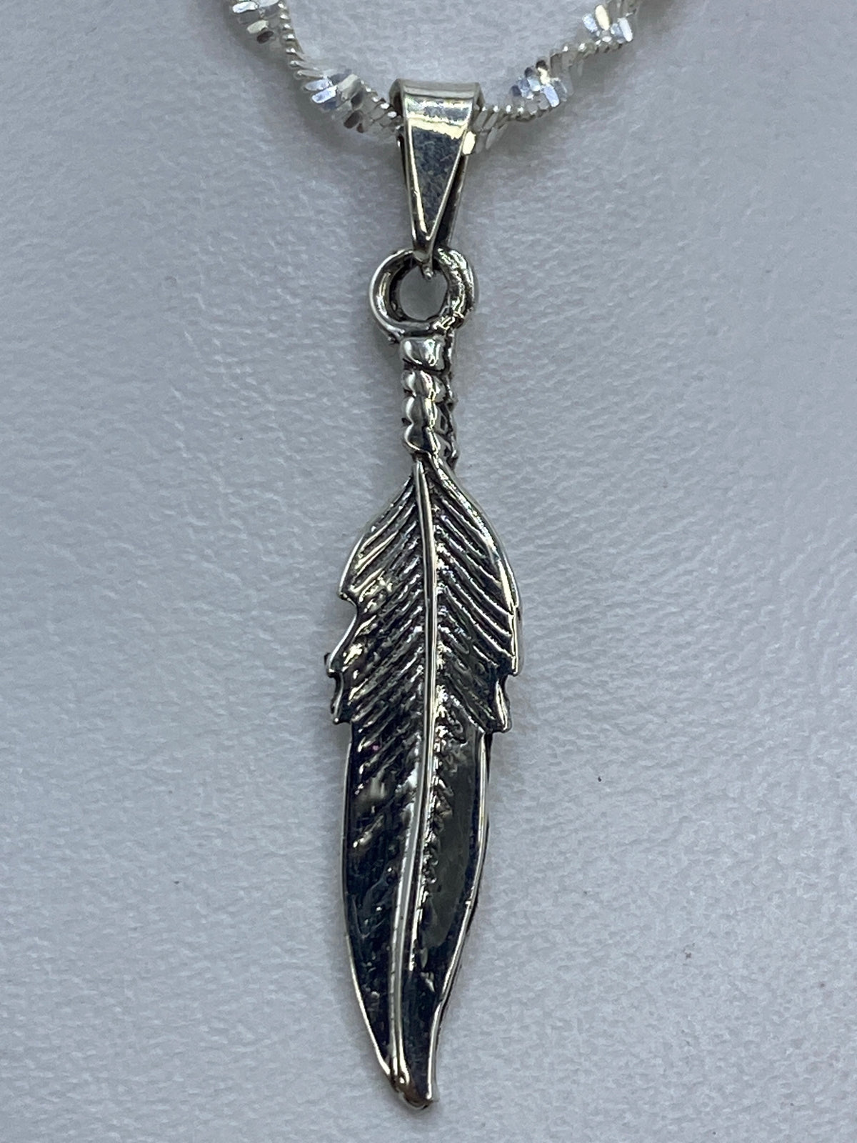 Dije de pluma de 4 cm de largo sobre regla de centímetros