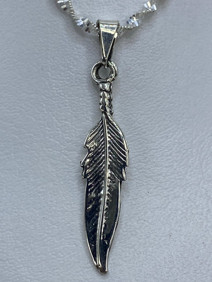 Dije de pluma de 4 cm de largo sobre regla de centímetros