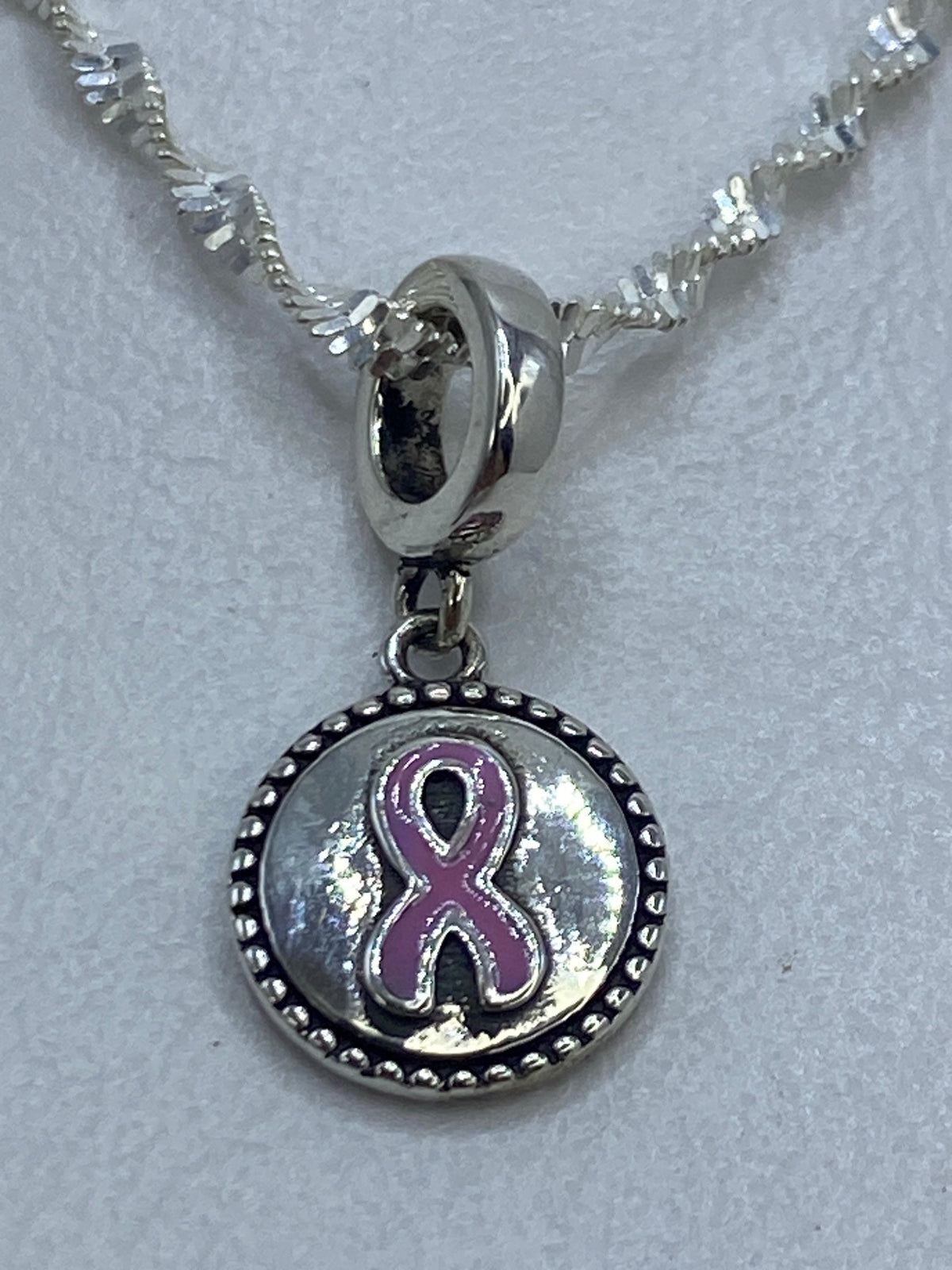 Dije de plata símbolo de conciencia en tono plateado, junto a cadena de plata en espiral