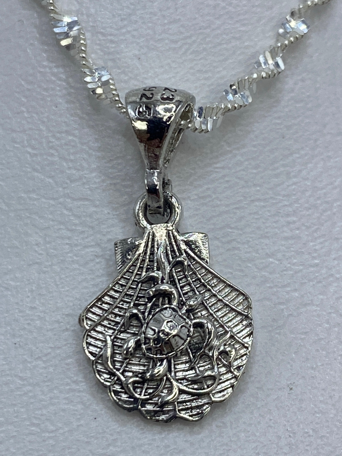 Dije de plata en forma de concha con detalles calados, colgante sobre fondo blanco