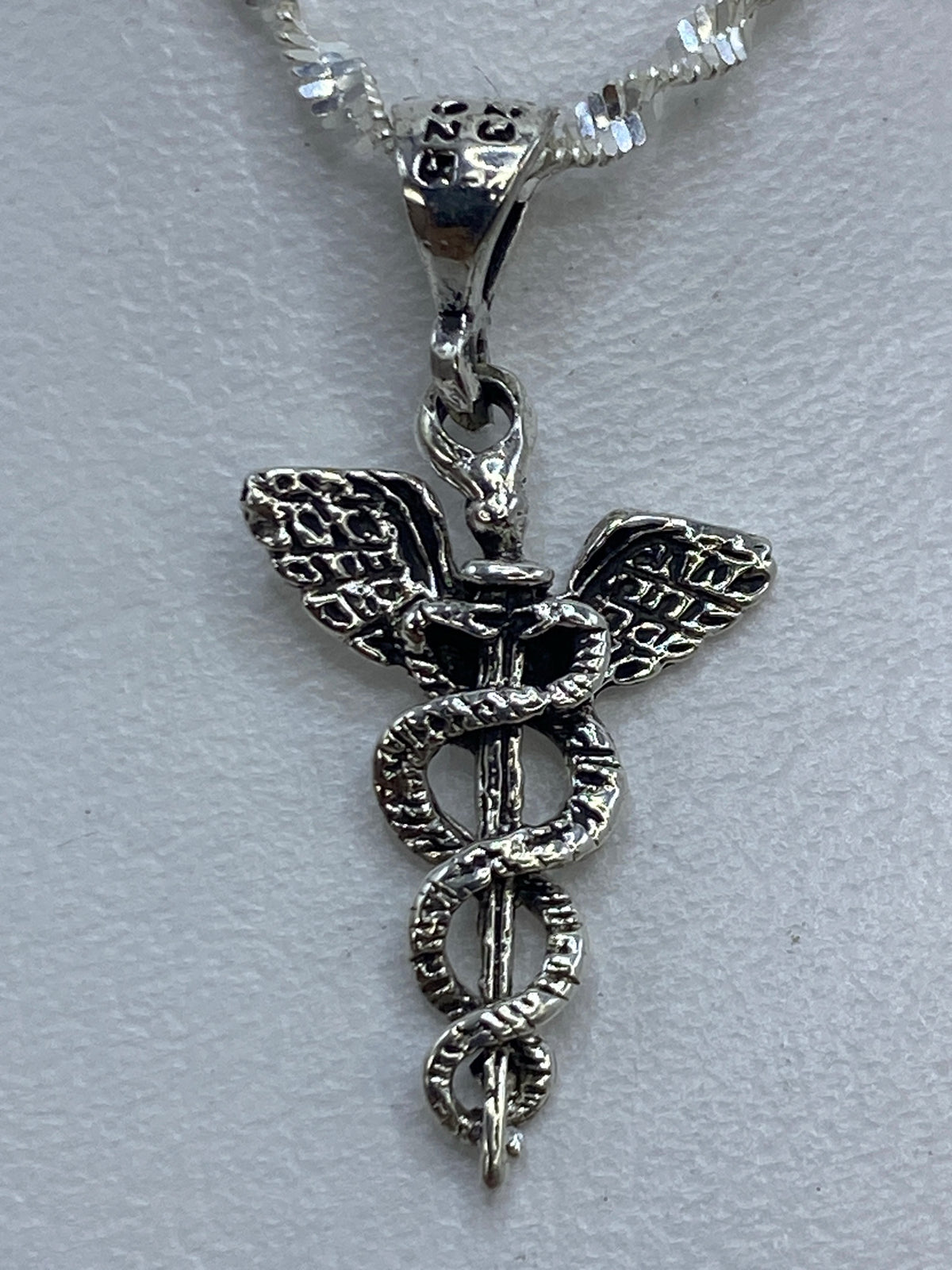 Dije caduceo de 3 cm sobre fondo blanco con sello .925 visible