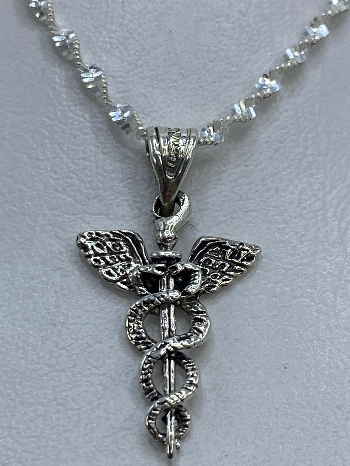 Dije de plata caduceo médico de 2 cm sobre fondo gris