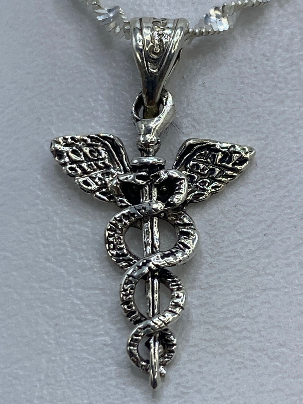 Dije caduceo en mano mostrando el tamaño real junto a regla centimétrica