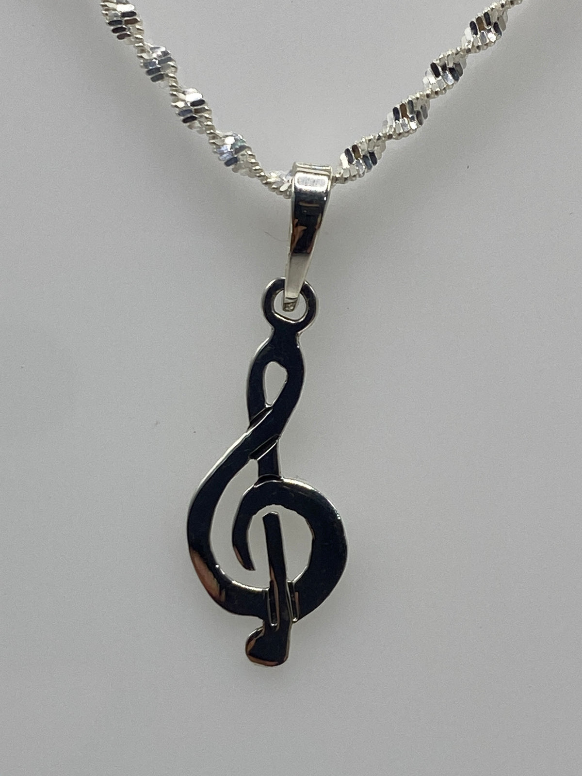 Dije de plata con clave de sol en calado, colgando de una cadena plateada