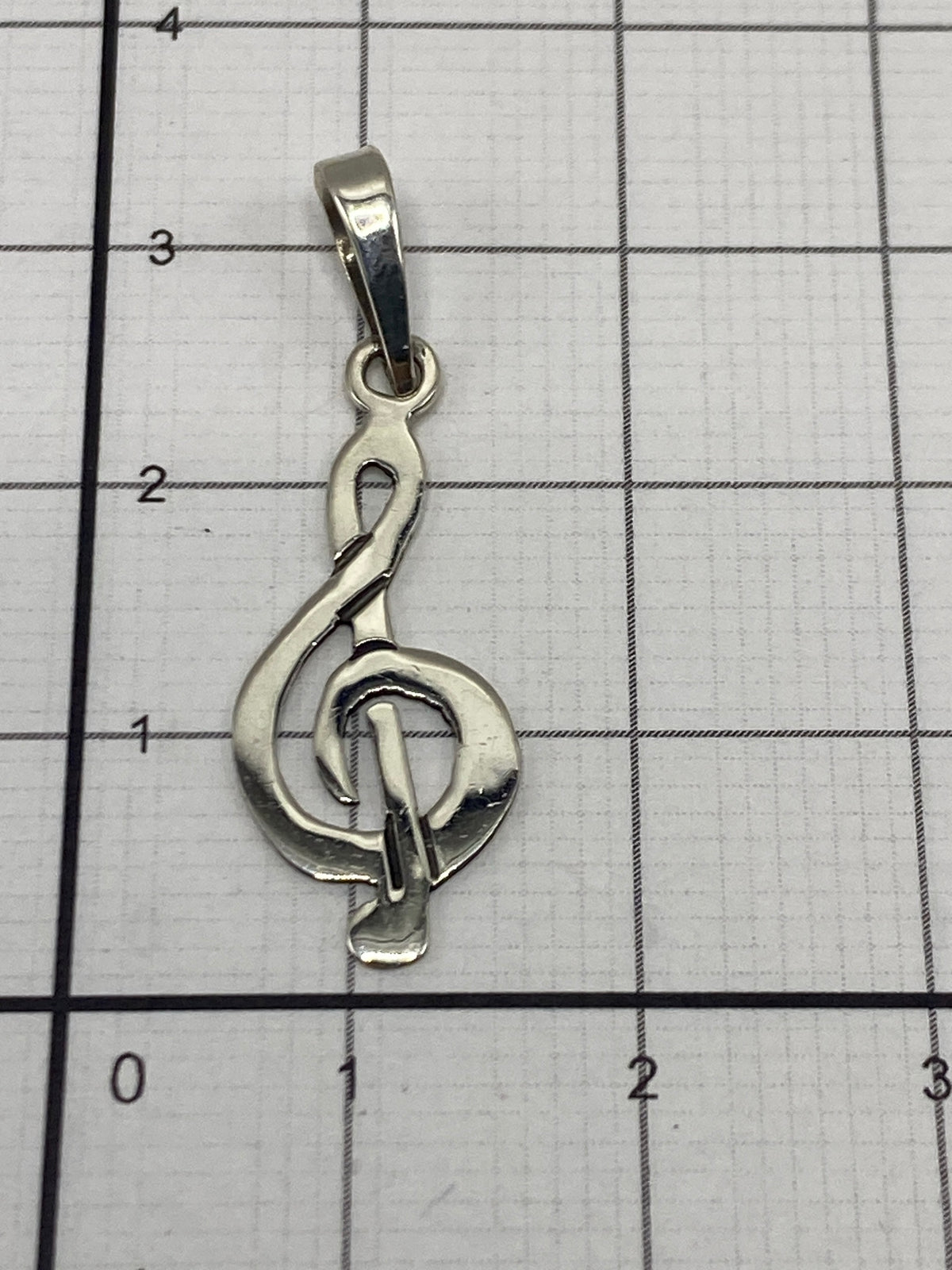 Dije de clave de sol en plata sobre escala de precisión mostrando peso de 0.6 gramos