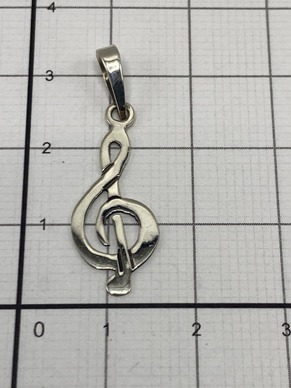 Dije de clave de sol en plata sobre escala de precisión mostrando peso de 0.6 gramos