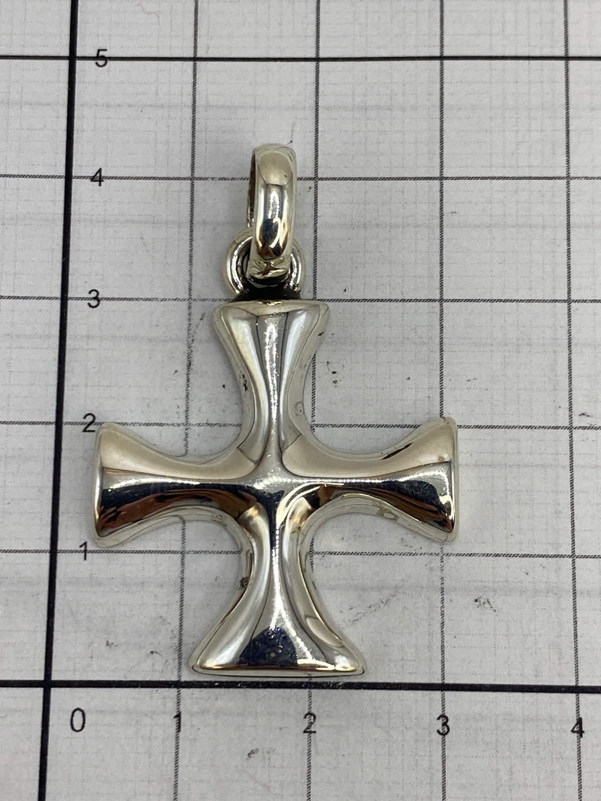 Dije cruz de plata sobre escala de centímetros