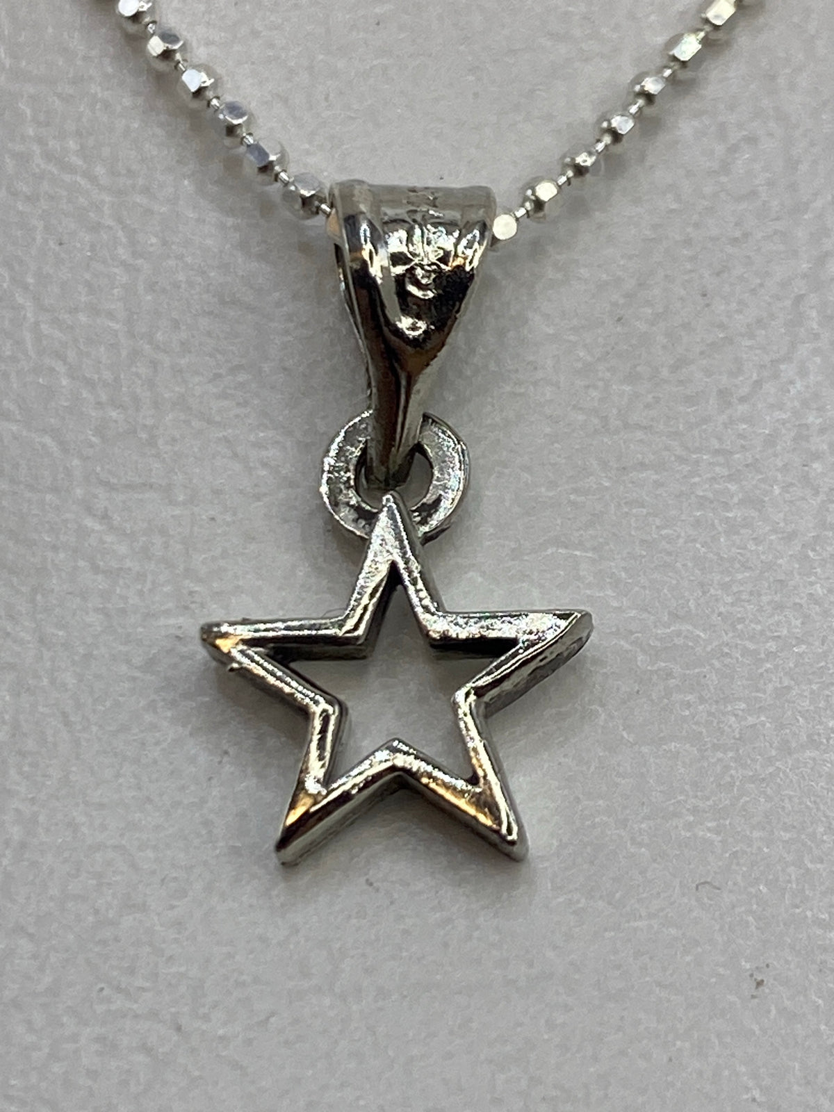 Dije de plata en forma de estrella abierta, calado, colgando de una cadena de bolitas