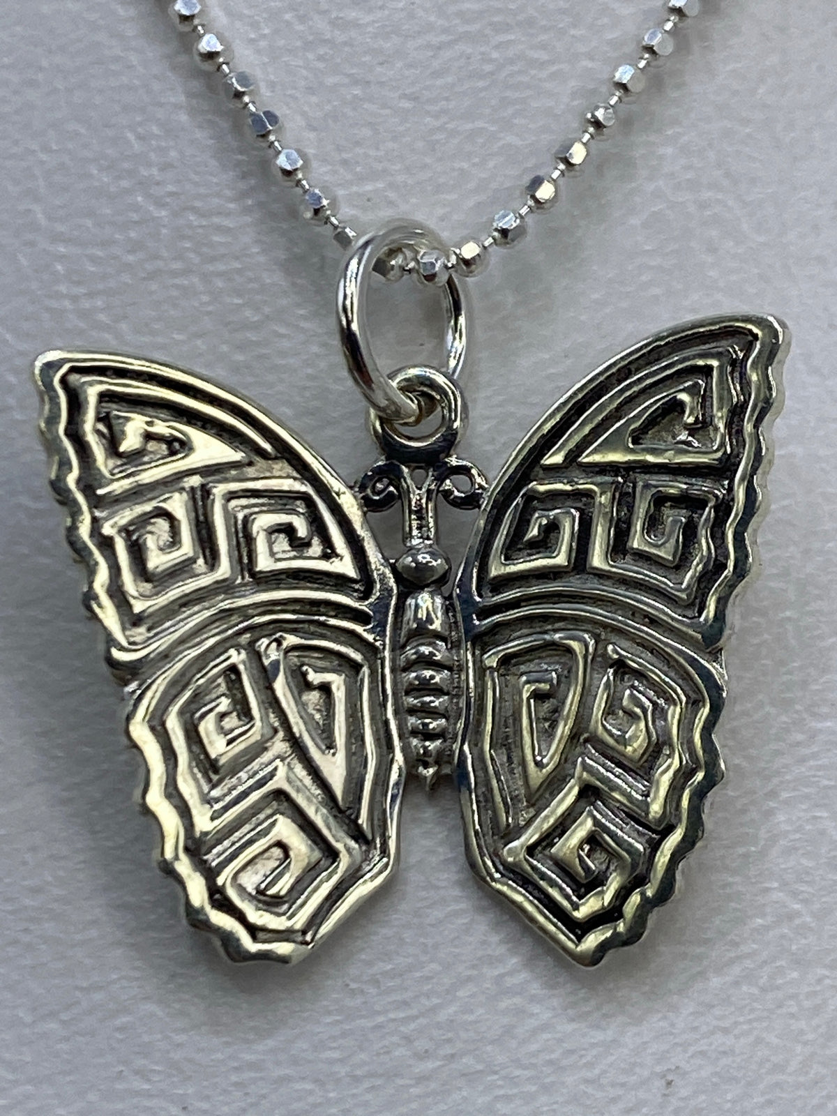 Dije mariposa de plata 950 sobre regla mostrando tamaño de 2 cm