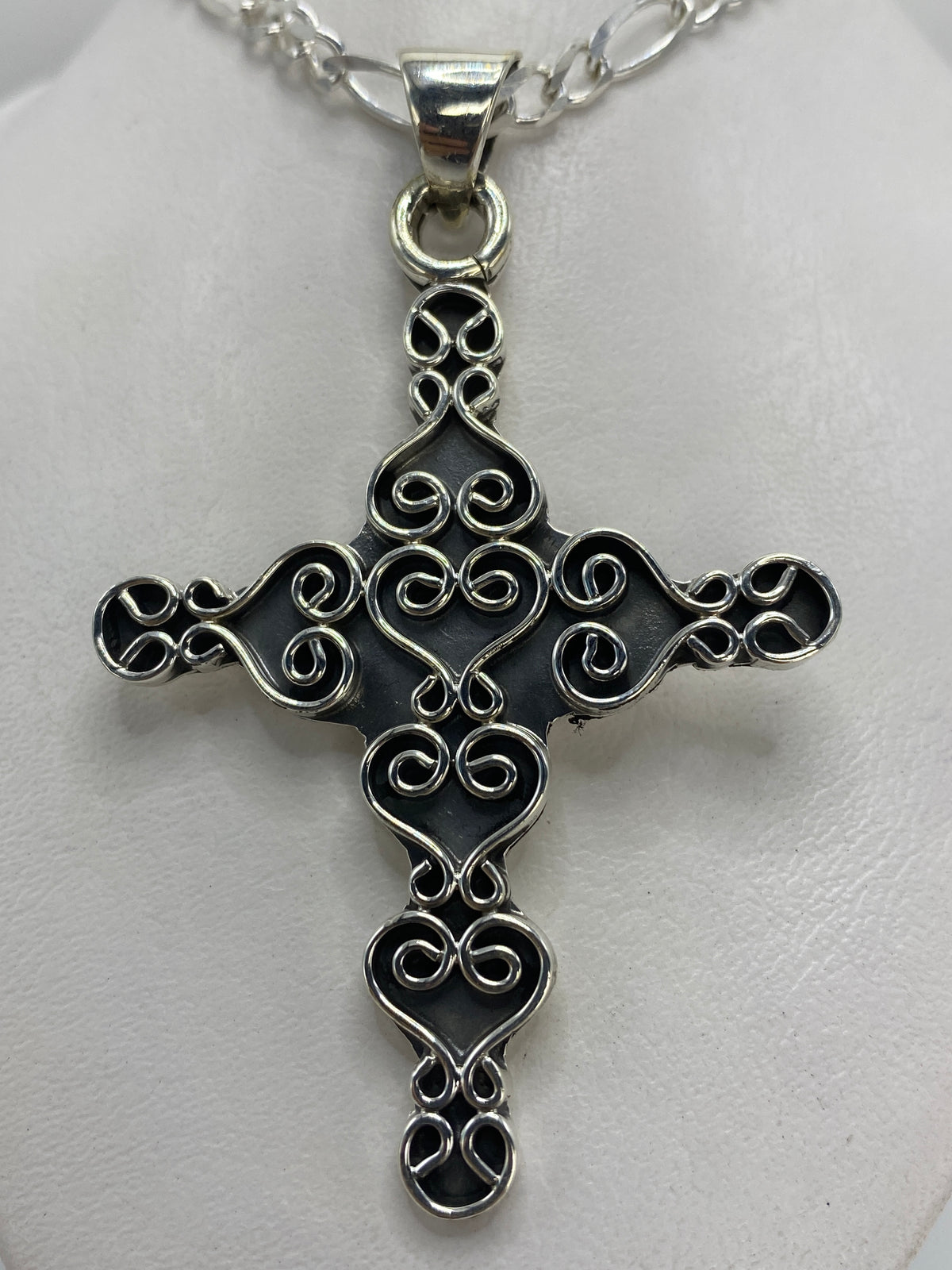 Vista frontal del dije cruz de 6.8 cm mostrando el diseño ornamentado con corazones