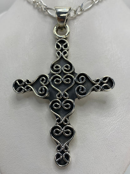 Vista frontal del dije cruz de 6.8 cm mostrando el diseño ornamentado con corazones