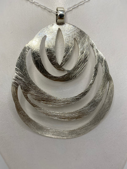 Vista frontal del dije de plata mostrando las cuatro capas geométricas con efecto bruñido